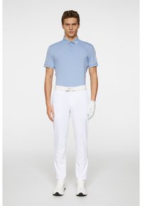 Koszulka polo w jasnoniebieskim kolorze, z krótkim rękawem, z trzema guzikami; zestawiona z białymi spodniami, białym paskiem i białymi trampkami. Widoczna ręka w rękawiczce.