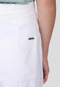 Shorts en denim blanc avec une large ceinture, comportant une poche arrière et une petite étiquette de marque en or sur la couture de la poche.