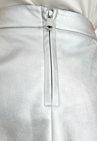 Silverfärgad faux läderkjol med en central dragkedjestängning och en elegant, slät textur med subtil lyster och sömdetaljer.