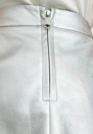 Jupe en simili cuir argenté avec fermeture zippée centrale, texture lisse et élégante, avec un léger éclat et des détails de couture subtils.
