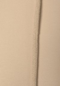 Tessuto beige a coste con una trama intrecciata lungo la cucitura, che mostra una superficie liscia e cuciture dettagliate.