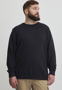 Fekete kereknyakú pulóver, puha anyagból készült, laza fitneszberendezéssel, bordás mandzsettákkal és hemével, valamint egy kis logóval a mellkason.