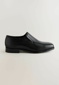Zapato negro de piel sin cordones con un diseño elegante y redondeado, textura suave y un sutil detalle de costura en la parte superior y los lados. Tacón plano.