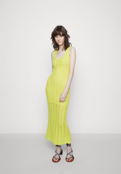 Vestido maxi de malha em amarelo neon brilhante, com corpete ajustado, padrão de malha aberta e barra com ponta. Emparelhado com sandálias castanhas de tiras.
