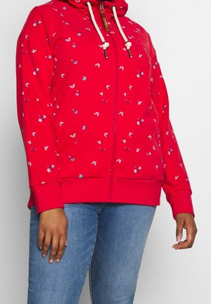 Red zip-up hoodie with small blue and white floral prints, white drawstrings, worn with light blue jeans.