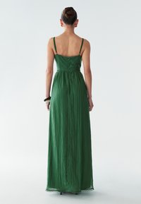 Garšs zaļš kleita ar plānām siksnām un pieguļošu jostasvietu. Audumam ir strukturēts, plūstošs raksts, ar viļņotu apakšmalu un aizmugurēju detaļu.