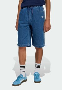 Shorts di jeans in blu medio, fascia elastica in vita con coulisse, tasche laterali, orli rifiniti. Abbinati a sneakers azzurro chiaro e calzini a righe.