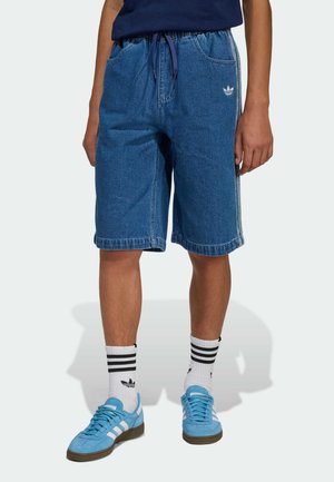 Krótkie spodenki dżinsowe w średnim odcieniu niebieskiego, elastyczna talia ze sznurkiem, boczne kieszenie, wykończone brzegi. Połączone z jasnoniebieskimi trampkami i skarpetkami w paski.