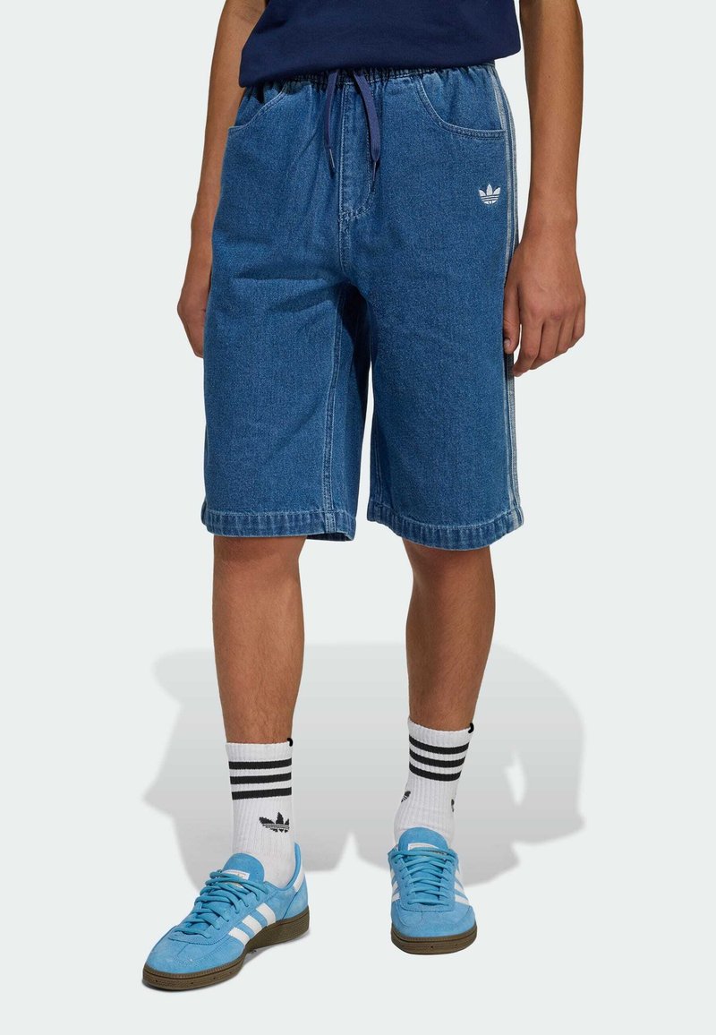 Shorts di jeans in blu medio, fascia elastica in vita con coulisse, tasche laterali, orli rifiniti. Abbinati a sneakers azzurro chiaro e calzini a righe.