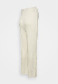 Calças largas de malha canelada em bege claro com uma cintura lisa e um padrão texturizado, que se estendem até o comprimento do tornozelo.