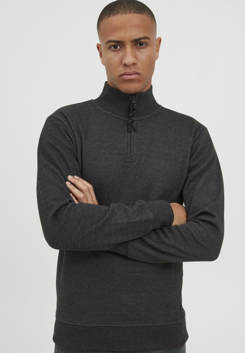 Hanorac zip-up de culoare gri închis, cu guler înalt, material texturat și fără modele vizibile. Manșon lung și o croială strânsă în talie.