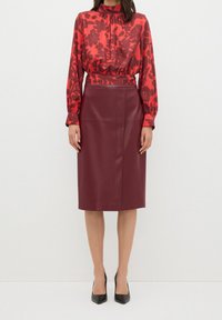 Rød bluse med blomsterprint, høj hals og lange ærmer, parret med en bordeaux farvet pencil nederdel i kunstlæder. Sorte højhælede sko.