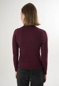 Marl bordeaux langærmet top med rund halsudskæring. Figursyet design og glat tekstur. Kombineret med højtaljede sorte jeans.
