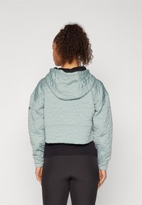 Giacca corta e soffice di colore azzurro, con texture trapuntata, cappuccio e polsini elastici, indossata sopra un top nero e leggings neri.