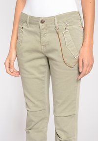 Ljust olivgröna byxor med rak skärning, två framfickor och en fastsatt dekorativ pärlband. Tillverkade av bomull med subtil textur.