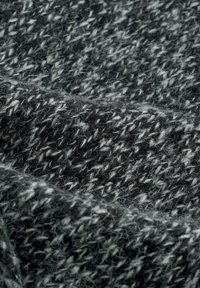 Grå och vit stickad tyg med en texturerad, mjuk yta; innehåller en blandning av mörka och ljusa trådar i ett fiskbensmönster.