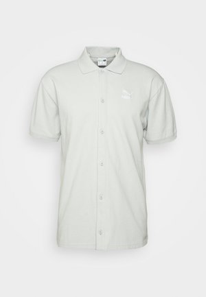 Šviesiai pilkos spalvos polo marškiniai, pagaminti iš medvilnės, su užsegimu priekyje, trumpomis rankovėmis ir baltu logotipu kairėje krūtinės pusėje. Minkšta tekstūra.