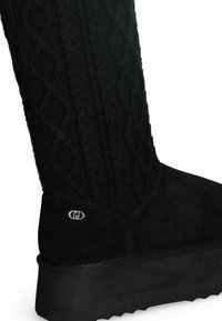 Bota negra hasta la rodilla con parte superior de punto texturizado, parte inferior de ante, detalle del logotipo y suela gruesa y texturizada.