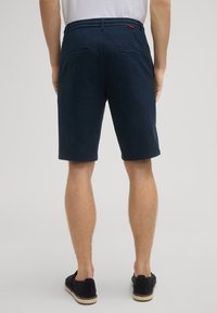 Shorts blu navy testurizzati con una cintura leggermente elastica, due tasche posteriori e un design minimalista. Indossati con scarpe slip-on scure.