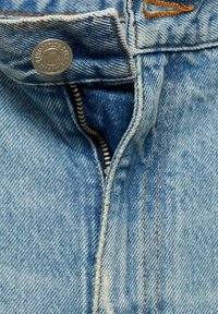Light blue denim fabric, featuring a metal button, a zipper closure, and orange-brown stitching along the seams and edges.