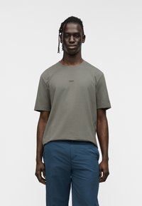 Ελιά πράσινο t-shirt με κοντά μανίκια από μείγμα βαμβακιού, με στρογγυλή λαιμόκοψη και διακριτικό λογότυπο 'BOSS' στο κέντρο. Το μοντέλο φοράει μπλε παντελόνι.