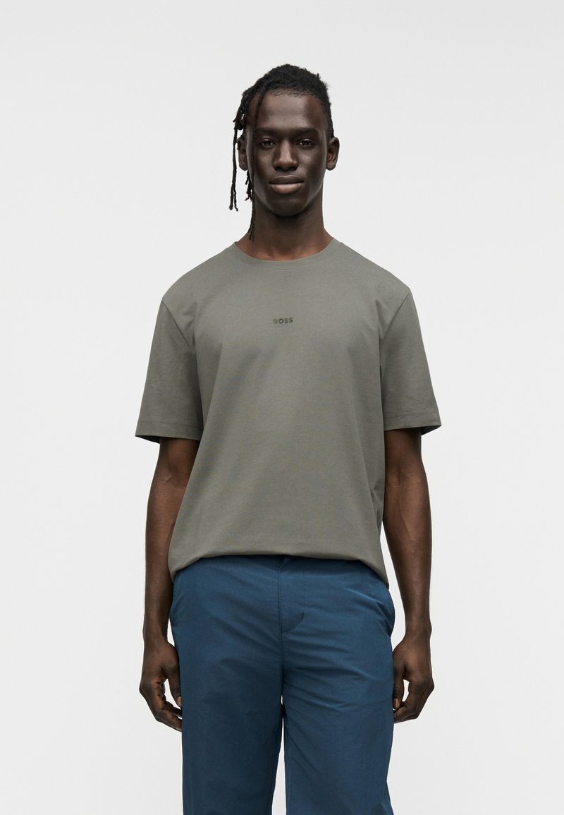 Ελιά πράσινο t-shirt με κοντά μανίκια από μείγμα βαμβακιού, με στρογγυλή λαιμόκοψη και διακριτικό λογότυπο 'BOSS' στο κέντρο. Το μοντέλο φοράει μπλε παντελόνι.