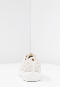 Baskets beiges faciles à enfiler avec motif logo MK et semelle en caoutchouc blanche. Présente une tige texturée et un accent doré à l'arrière.