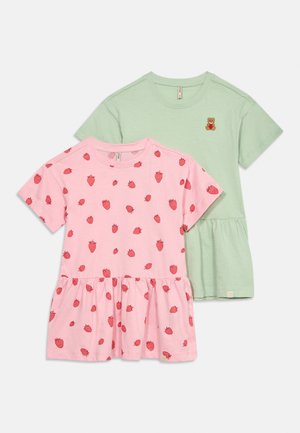 Due vestitini per bambini piccoli a maniche corte, uno rosa con stampe rosse di fragole, uno verde chiaro con una piccola toppa a forma di orsetto, entrambi con gonne arricciate.