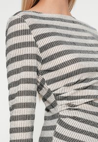 Pasek długa bluzka z długim rękawem w czarne i kremowe poziome paski, z prążkowaną teksturą i dopasowanym krojem. Okrągły dekolt, brak widocznych elementów metalowych.