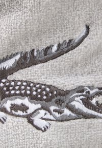 Tessuto grigio texturizzato con un dettagliato design di un coccodrillo ricamato in bianco e nero, con squame decorate e tratti facciali distintivi.