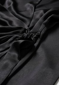 Tissu gris foncé avec un détail froncé rassemblé créant des plis doux et une texture sur une surface lisse.