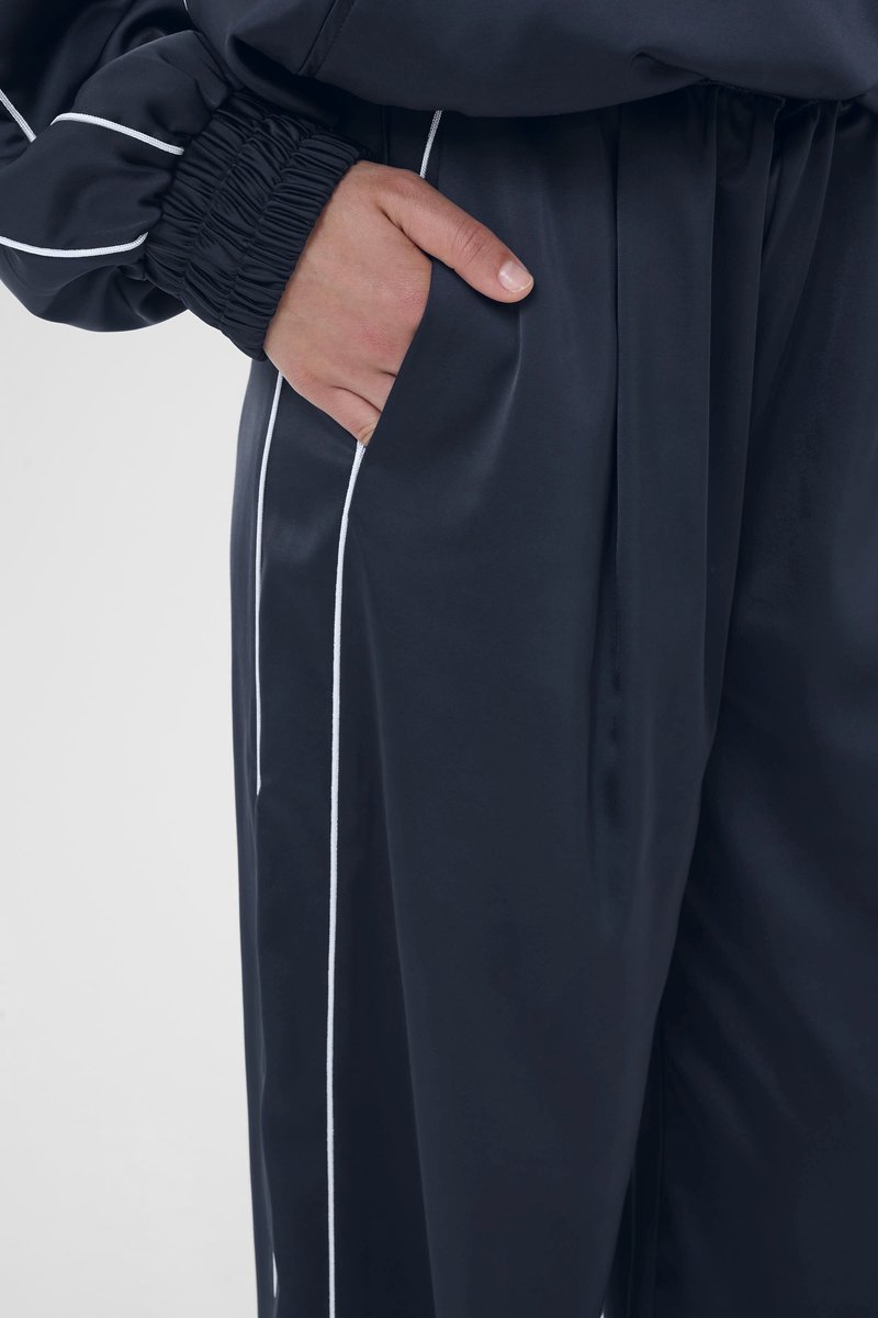 Marineblaue Jogginghose aus glattem Stoff, mit weißem Paspel entlang der Seite. Elastischer Bund mit Tasche auf der rechten Seite.