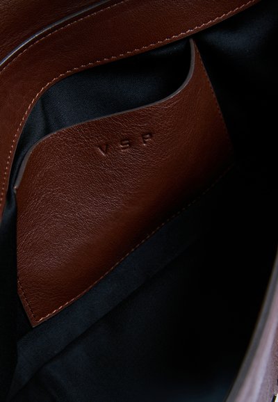 Gros plan d'une poche intérieure en cuir marron avec les lettres en relief VSP sur fond en tissu noir.