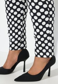 Zwarte high heels met een puntige neus, gecombineerd met zwart-witte polkadotsbroek, gemaakt van een gladde stof en met een slim fit.