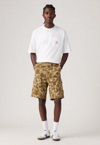 White crew neck t-shirt with a chest pocket, paired with camo-pattern cargo shorts in green and brown. Worn with white socks and sneakers.