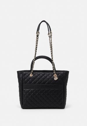 Black quilted tote bag with chain and leather handles, displaying an embossed "GUESS" logo on the front. Smooth texture with metallic accents.