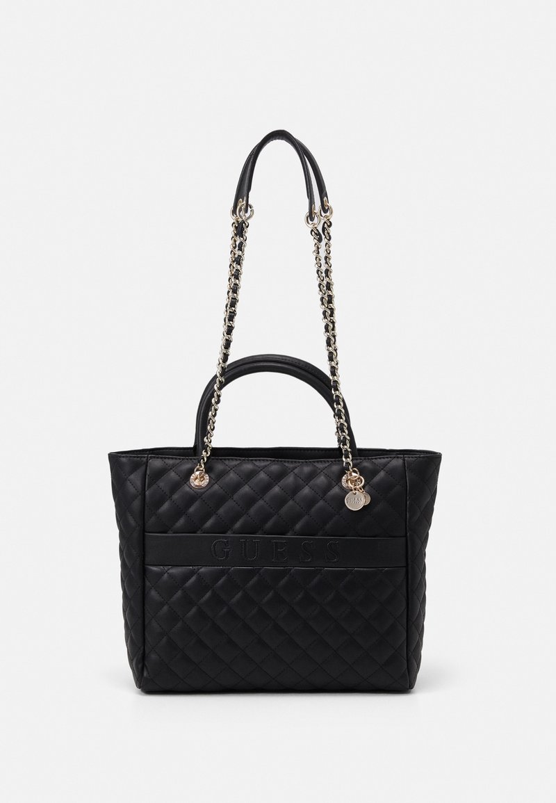 Sort quiltet tote taske med kæde- og læderhåndtag, der viser et præget "GUESS"-logo foran. Glat tekstur med metalliske accenter.