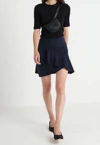 Haut noir à rayures avec manches courtes associé à une jupe bleu marine à volants, accessoirisé d'un petit sac à bandoulière noir et de talons noirs.