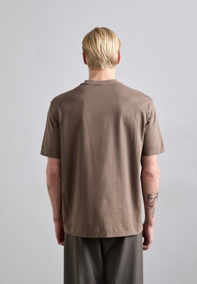 Camiseta de algodón marrón con un corte relajado, mangas cortas y cuello redondo. Textura suave y diseño liso sin patrones ni acentos visibles.