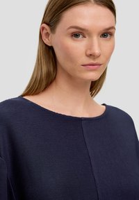 Marineblaue Bluse mit strukturierter Ripp-Oberfläche, Rundhalsausschnitt und kurzen Ärmeln; weist eine Nahtdetails für visuellen Reiz auf.