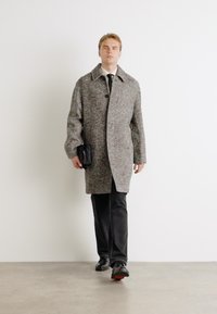 Palton gri din lână cu guler tip notch, închidere cu nasturi și mâneci încăpătoare. Purtați peste pantaloni negri, având o geantă mică în mână.