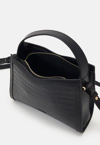 Sac à main noir avec texture crocodile, poignée supérieure et fermeture éclair dorée, montré partiellement ouvert sur un fond uni.