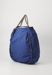 Grand sac à main bleu en tissu doux, doté de bretelles épaisses à motifs et d'une forme arrondie avec des coutures visibles.