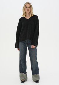 Maglione nero a collo a V con vestibilità ampia e maniche lunghe abbinato a jeans blu a gamba larga con orli sfilacciati e un accento in denim chiaro sui polsini.