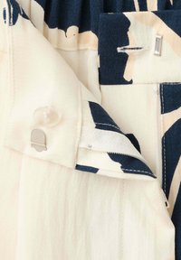 Gros plan d'un vêtement blanc et bleu marine à motif montrant un bouton, un fermoir crochet et une fermeture éclair partiellement ouverte.