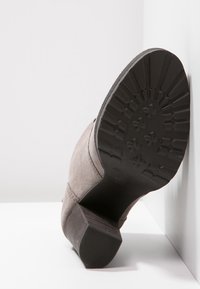 Gray suede ankle boot featuring a textured rubber sole, stacked heel, and seam detailing along the sides. View from the back.