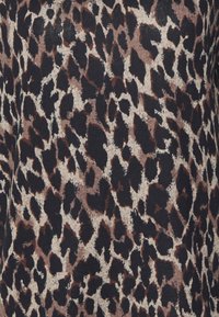 Leopardmönstrad tyg med svarta, bruna och beige nyanser. Texturen är mjuk och stickad, med oregelbundna fläckar på en ljus bakgrund.