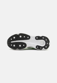 Suela de zapatilla en blanco y negro con un patrón de tracción texturizado y elementos de amortiguación. Presenta recortes circulares y acentos elevados para un mejor agarre.