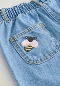 Pantalon en denim bleu clair avec une taille élastique et une petite poche arrière présentant une abeille brodée texturée avec des ailes roses.