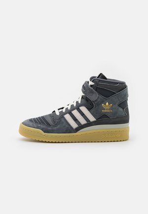 Baskets montantes Adidas grises avec des bandes et des lacets blancs, un logo doré et une semelle jaune moutarde, vues de côté.